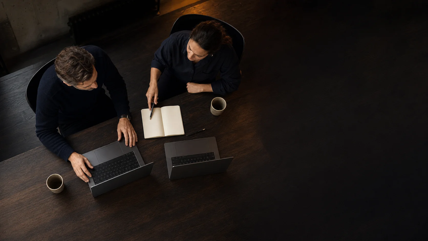 Bird's-eye editorial view of two Bench Operators collaborating beside open laptops with hidden screens